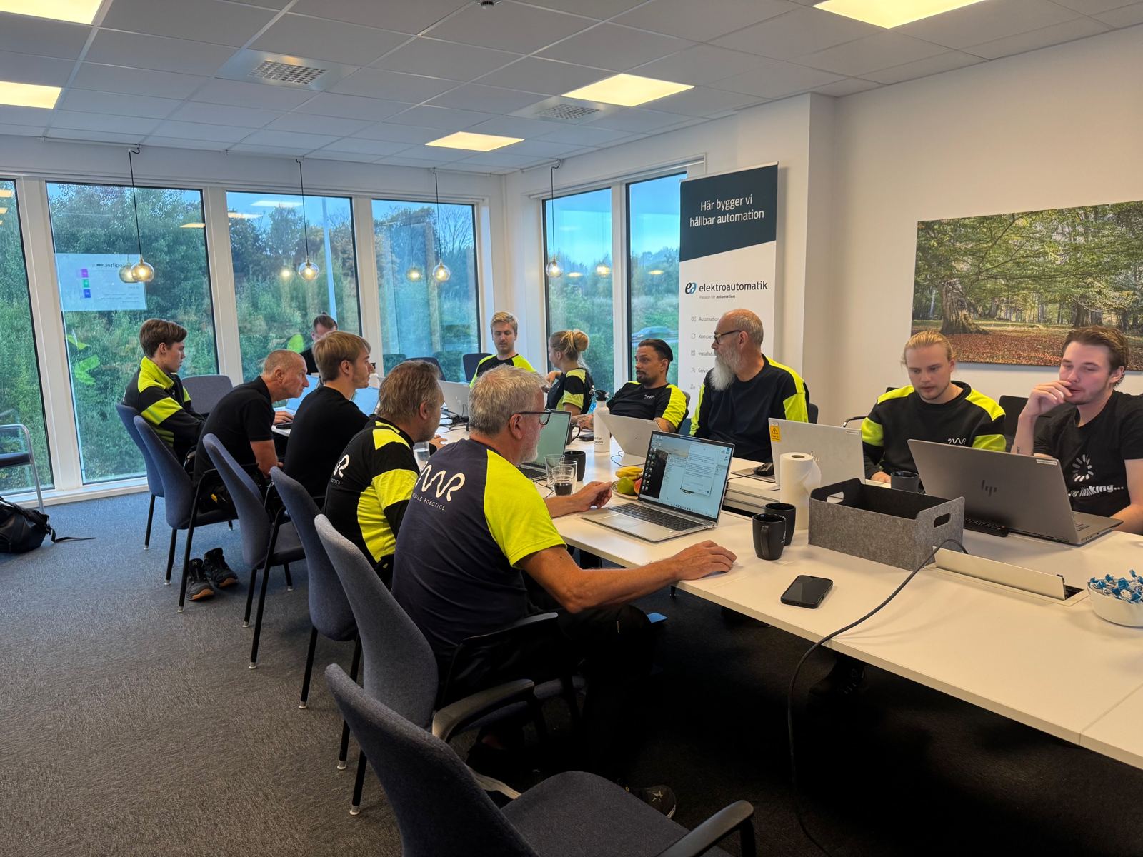 Deltagare sitter vid ett långbord med laptops och arbetar med övningar under en AI-workshop